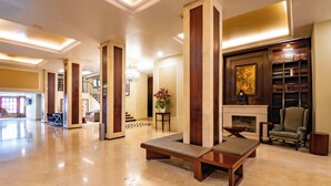 Un vestíbulo amplio con piso de mármol, chimenea, estantería y zona de estar con banca y sillones.