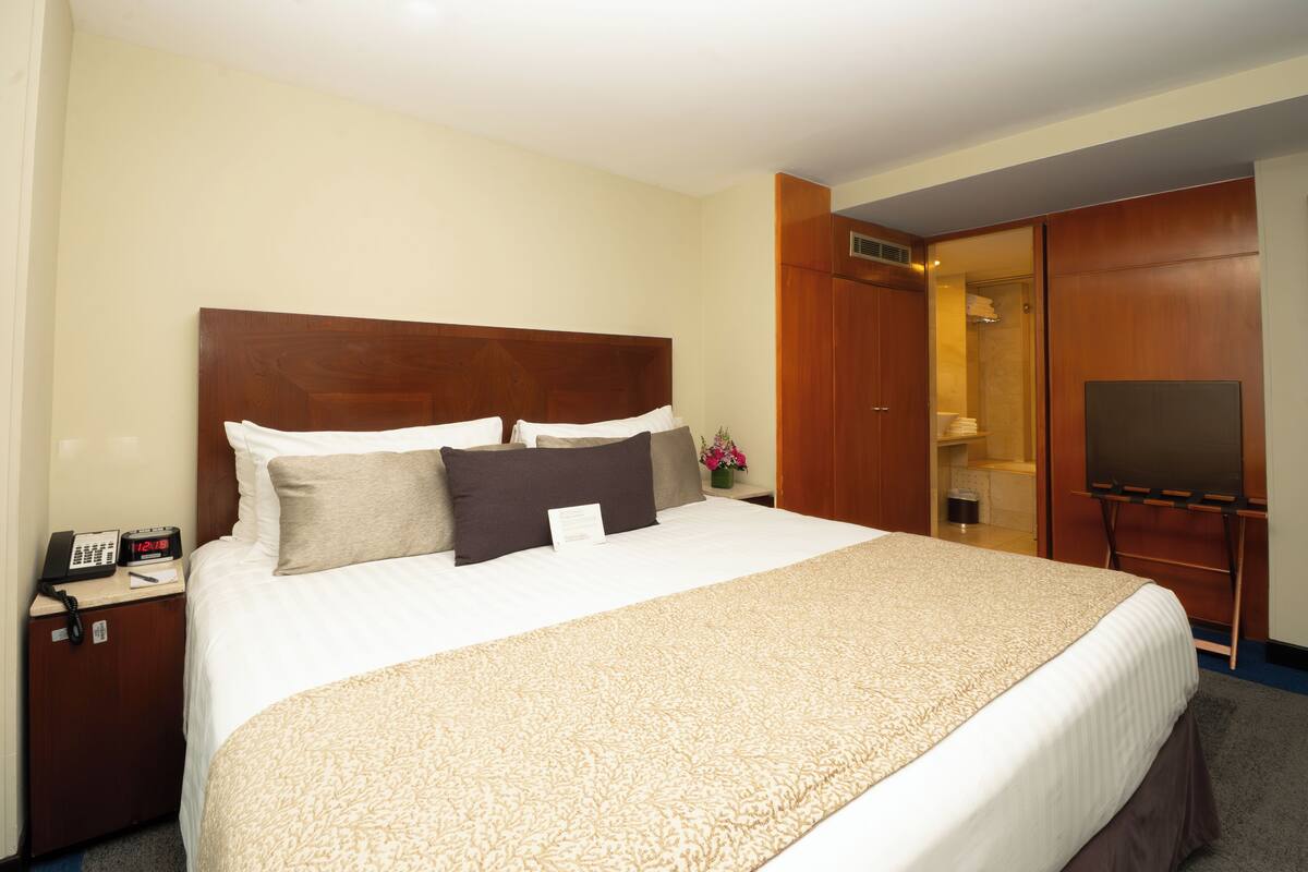 A hotel room with a large bed, a bedside telephone, a television, and a wardrobe.