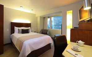 Relax in this inviting room with a city view, featuring a comfortable bed, a chair, and a table for a quiet moment with a cup of tea.