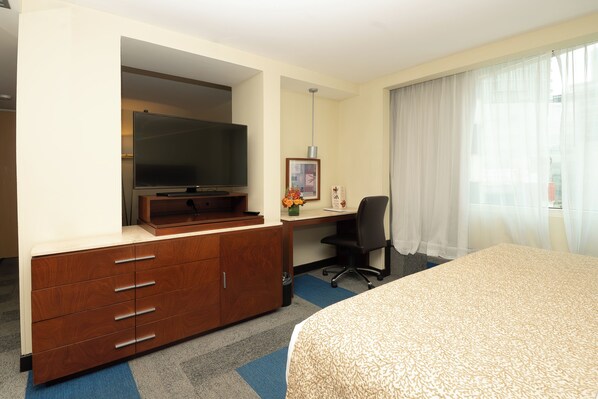 Habitación de hotel con cama, escritorio con computadora, televisor y armario.