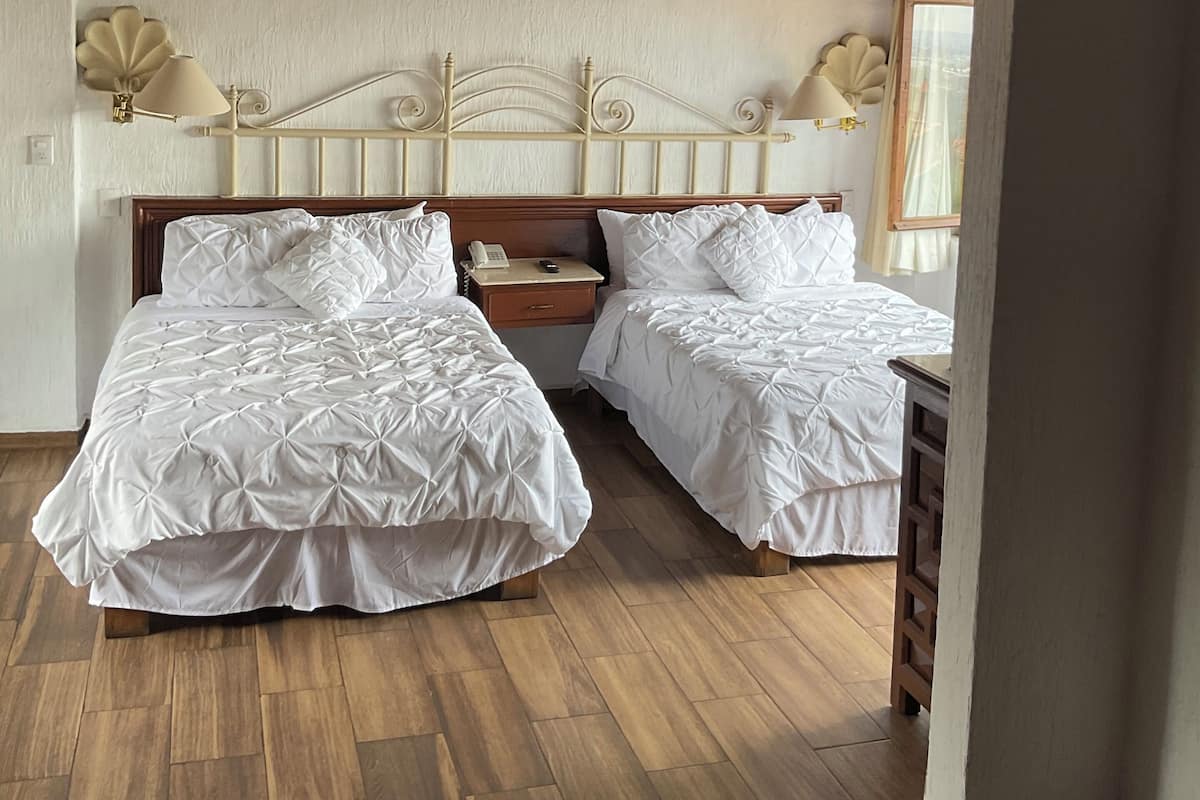 Une chambre avec deux lits, un plancher en bois, une tête de lit blanche, des lampes de chevet et une table de chevet en bois.