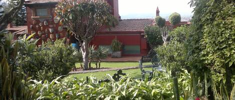 A red building with a tiled roof, surrounded by greenery and a garden.