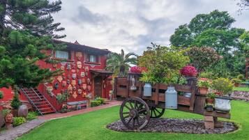 A red building with a mural of masks, a wooden fence with potted plants, and a stone pathway leading to a staircase.