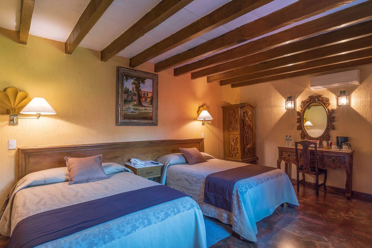 Une chambre d’hôtel avec deux lits, un bureau, une chaise, un miroir et un tableau au mur.