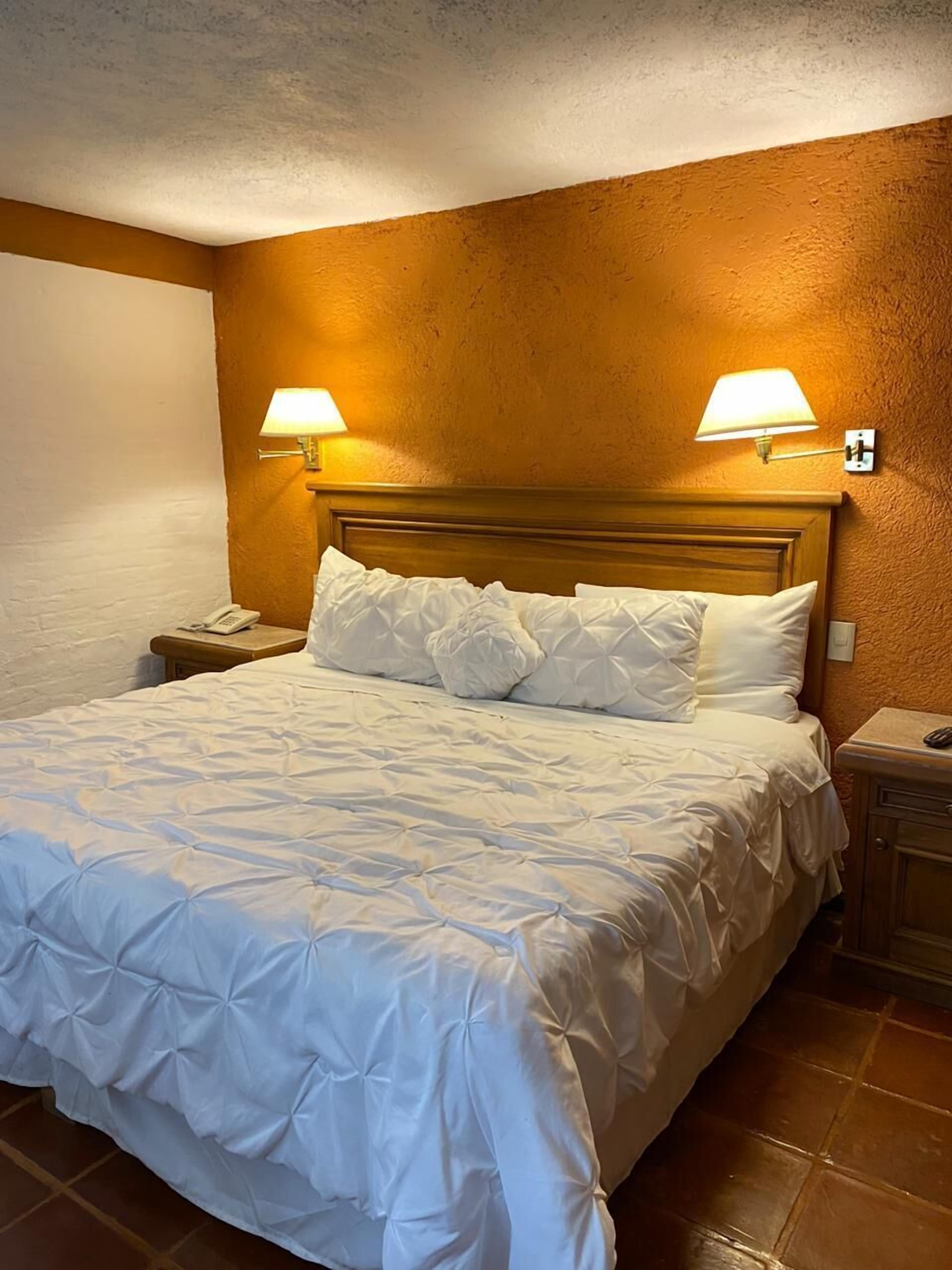 A neatly made bed with a wooden headboard, two bedside lamps, and a telephone on a nightstand.
