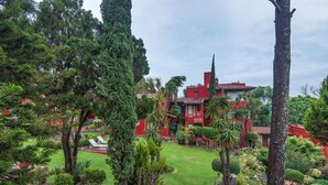 Een weelderige tuin met een rood gebouw, omgeven door diverse bomen en planten.