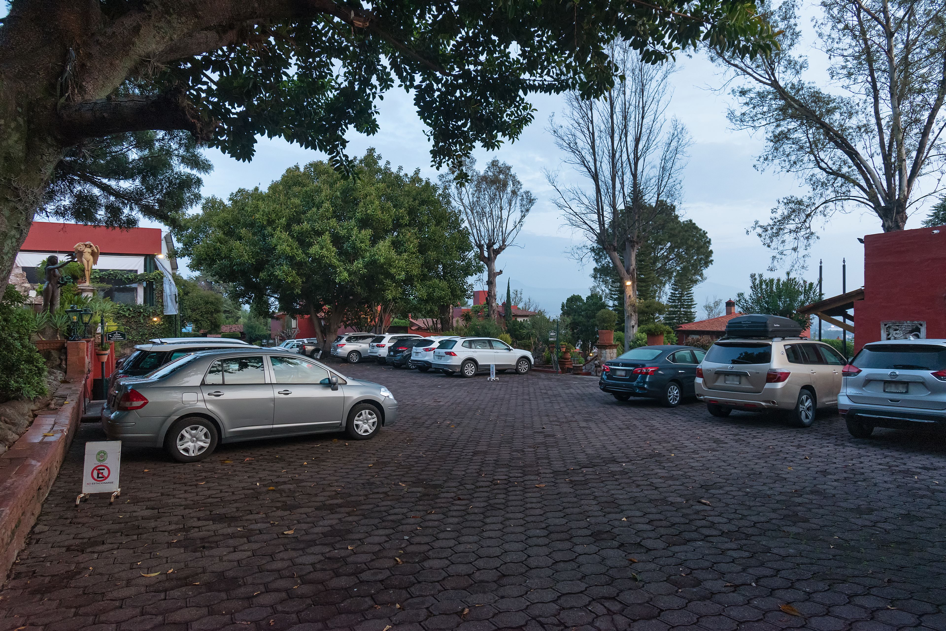 A parking area with multiple cars, trees, and buildings in the background.