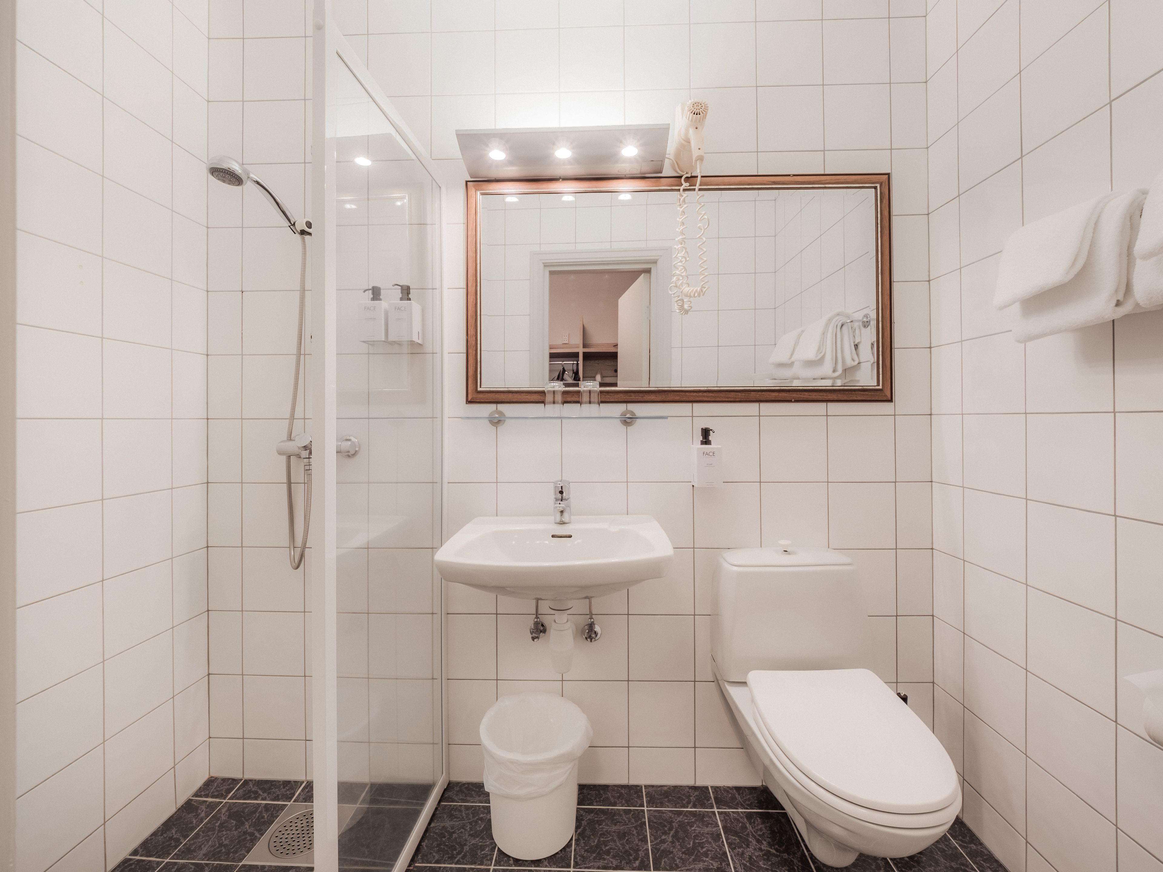 Een moderne badkamer met een douchecabine van glas, een wit wastafelmeubel, een toilet en een spiegel met houten lijst.