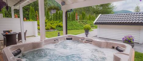 A hot tub under a covered patio with a view of a lush garden and a mountain in the background.