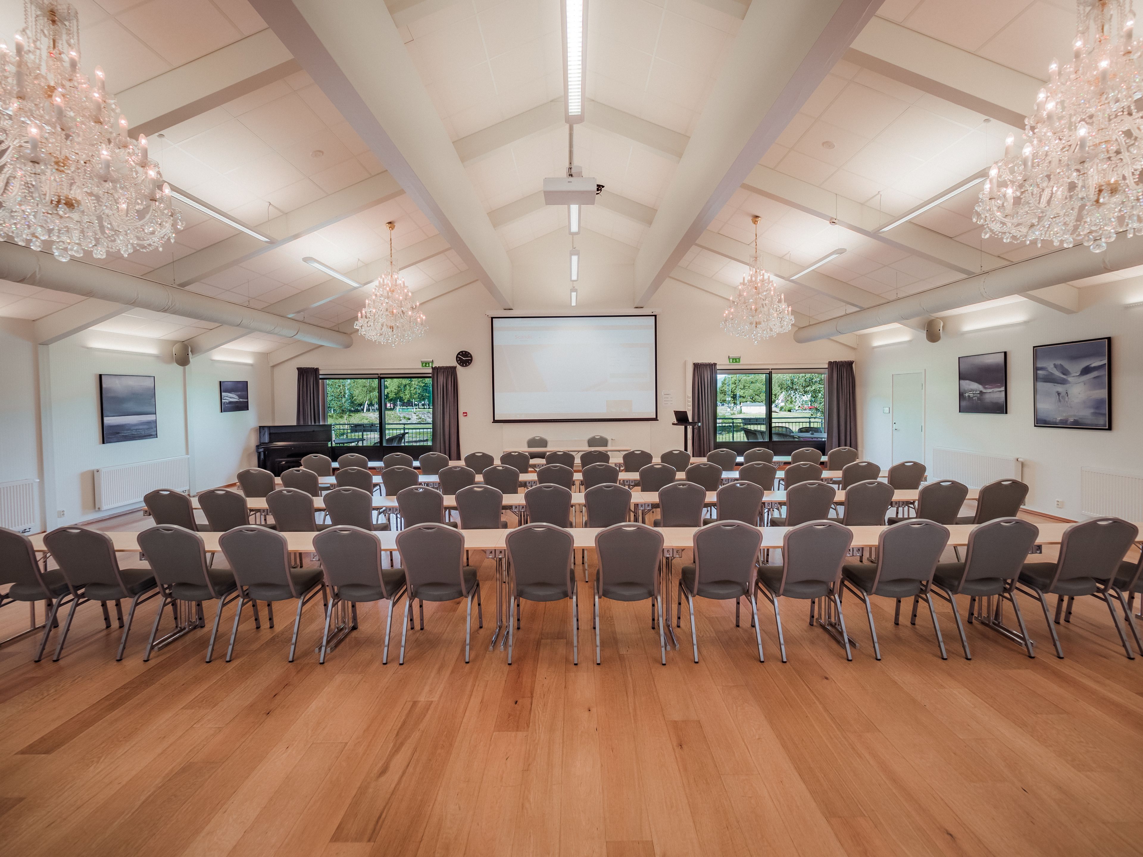 Un salón de conferencias con una pantalla grande, varias filas de sillas y candelabros.