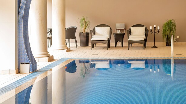 A swimming pool with a tiled edge, lounge chairs, a potted plant, and a candle holder. - Nordfjord Hotell (Stad)