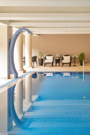 Una piscina con borde de azulejos, sillas de descanso, una planta en maceta y un candelabro.