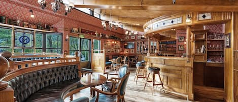 Angolo bar accogliente, con rivestimenti in legno, una panca a forma di ferro di cavallo e diversi sgabelli, circondato da librerie e quadri incorniciati.