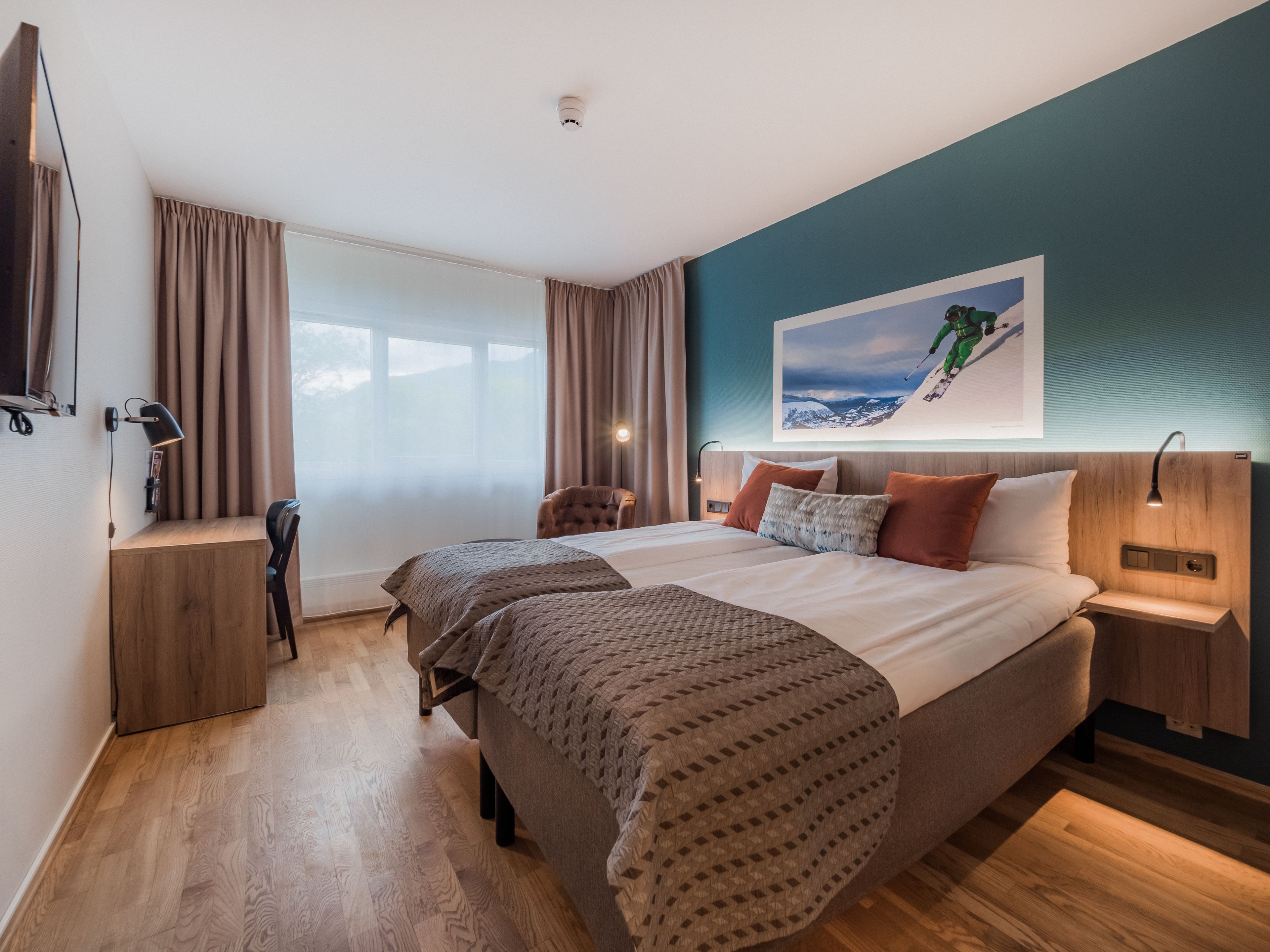 Una habitación de hotel moderna con una cama grande, dos mesitas de noche, un escritorio y una silla.