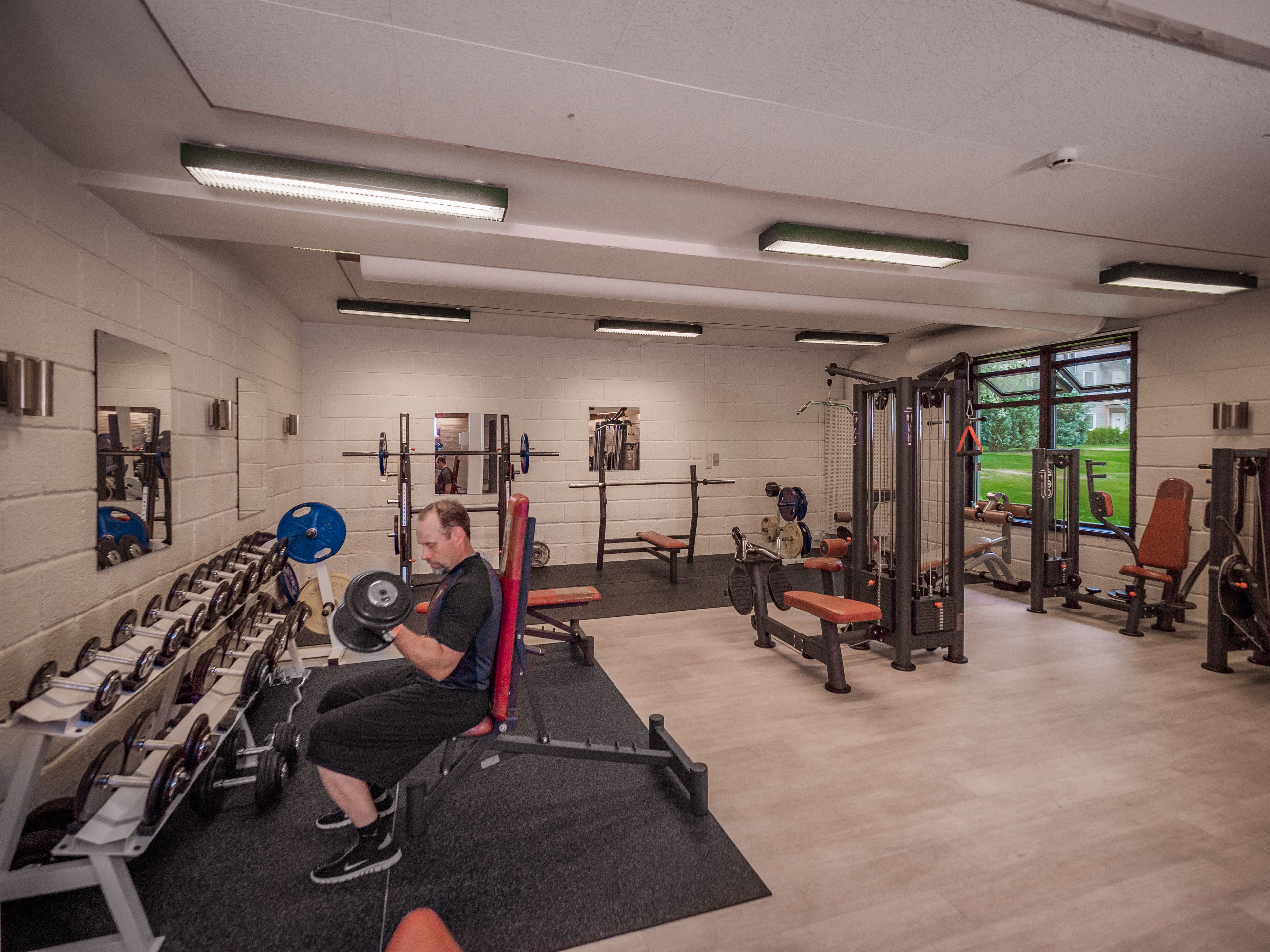 Une salle de sport équipée de matériel de musculation, de bancs et de miroirs aux murs.