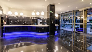 Un moderno vestíbulo de hotel con un mostrador de recepción, paredes de mármol y una barra iluminada en azul.