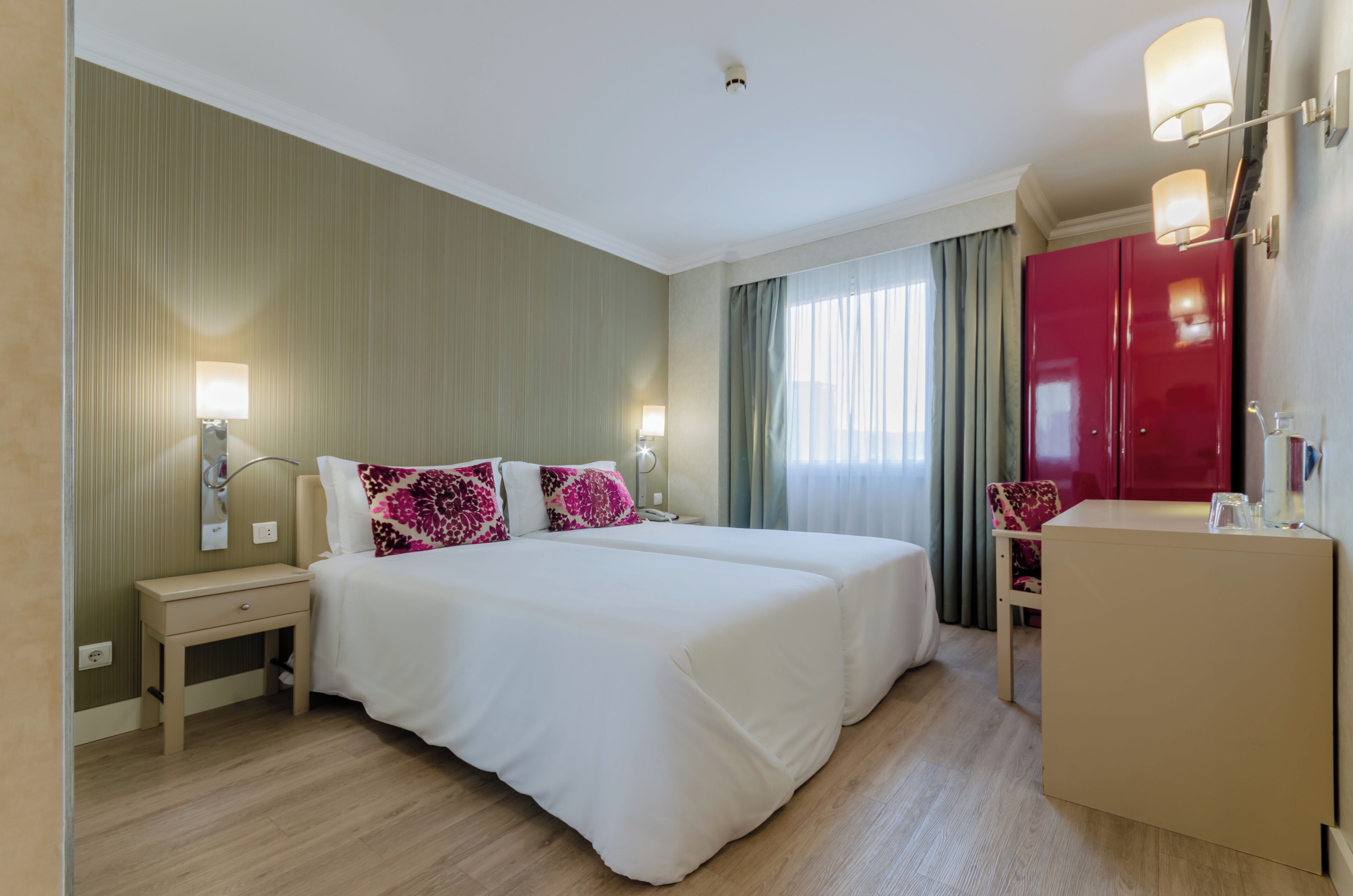 Una habitación de hotel con una cama grande, mesitas de noche, un escritorio, una silla, un armario y un espejo.