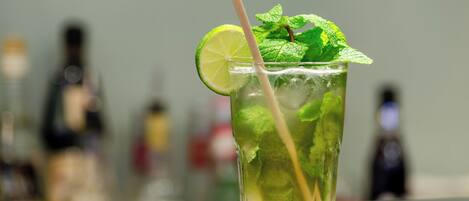 A glass of a green beverage with a lime slice and mint leaves, placed on a reflective surface.