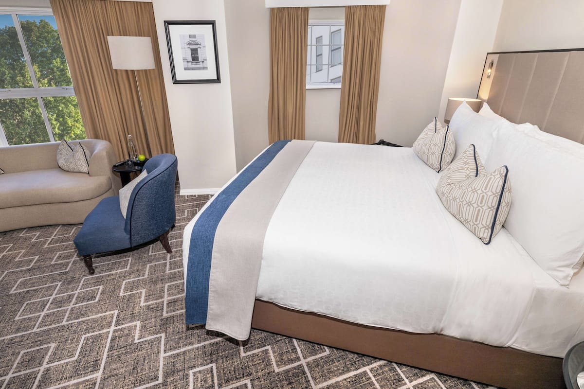A hotel room with a large bed, a sofa, a chair, and a window with curtains.