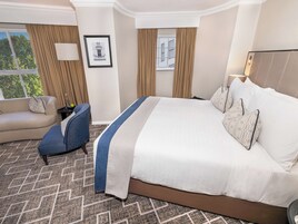 Una habitación de hotel con una cama grande, un sofá, una silla y una ventana con cortinas.