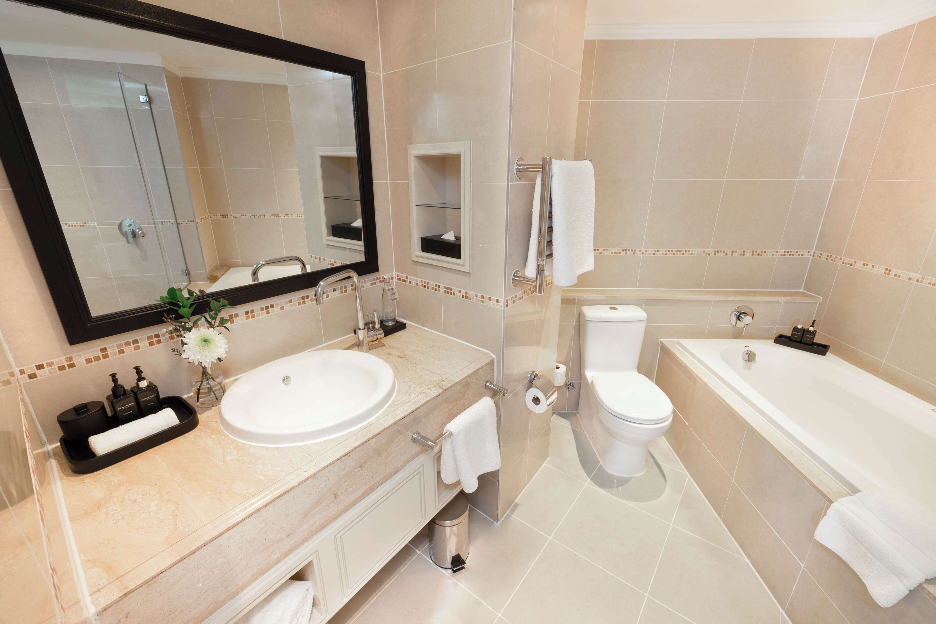 A modern bathroom with a large mirror, two sinks, a toilet, and a bathtub.