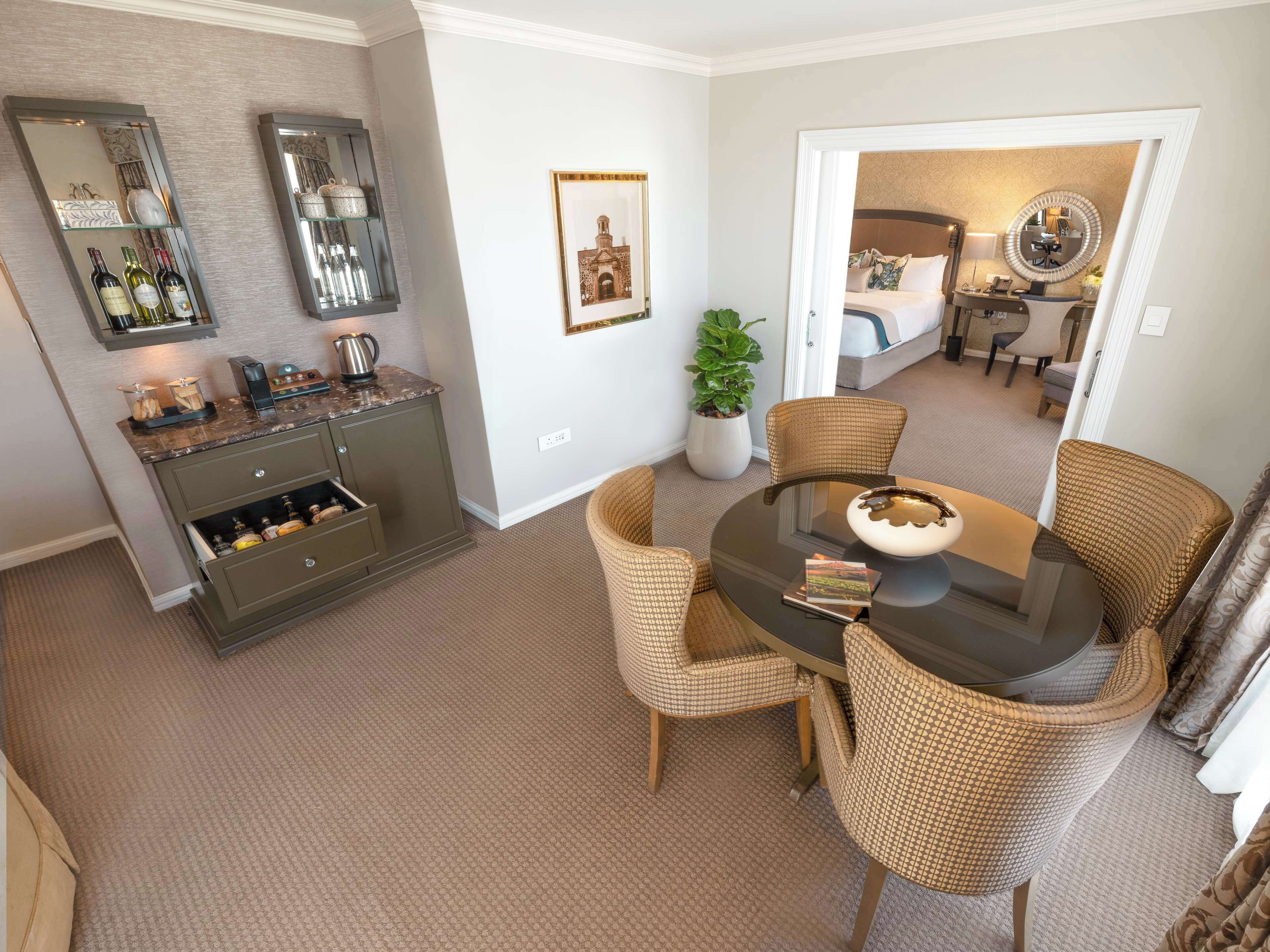 A compact living space with a dining area, a kitchen with wine bottles, and a potted plant.