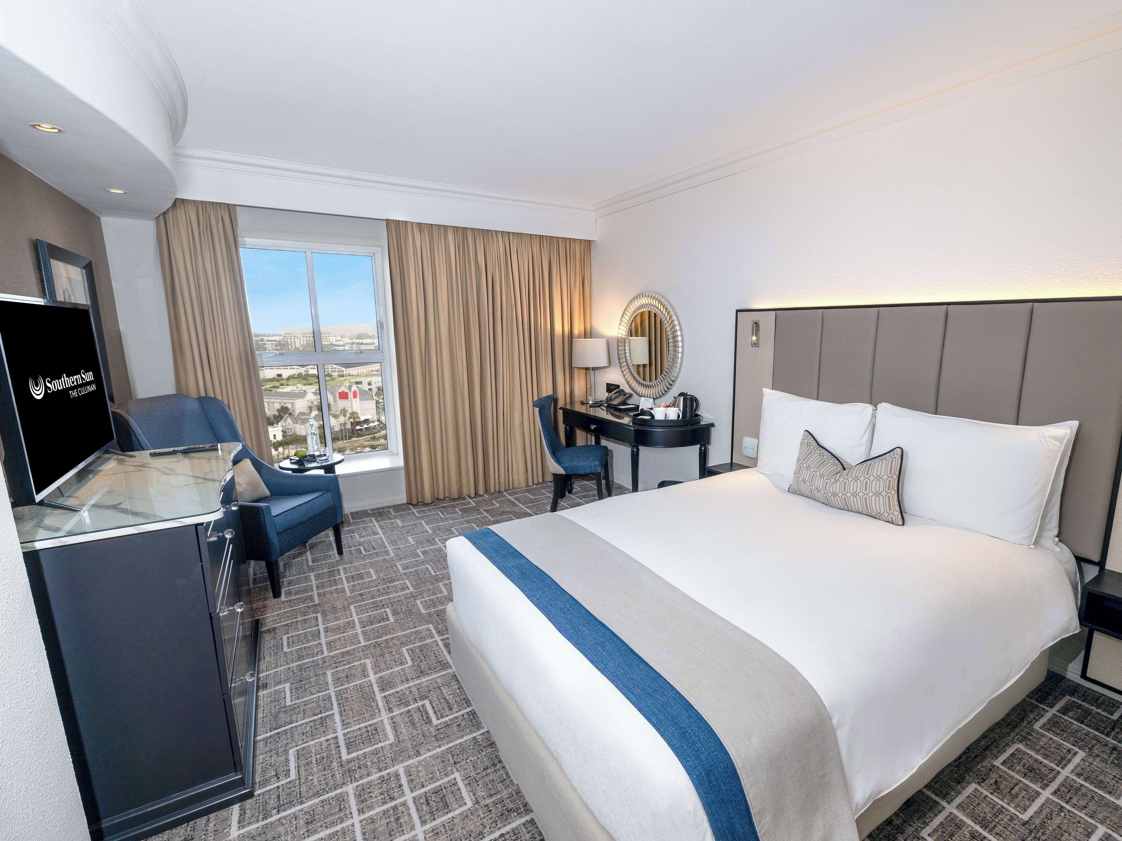 Hotelkamer met een groot bed, een bureau met stoel, een televisie en uitzicht op de stad.