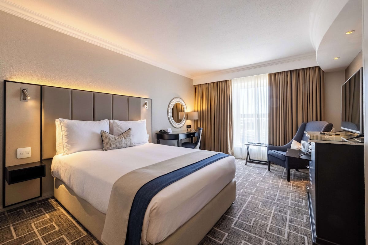A hotel room with a large bed, a desk, a chair, a TV, and a mirror.