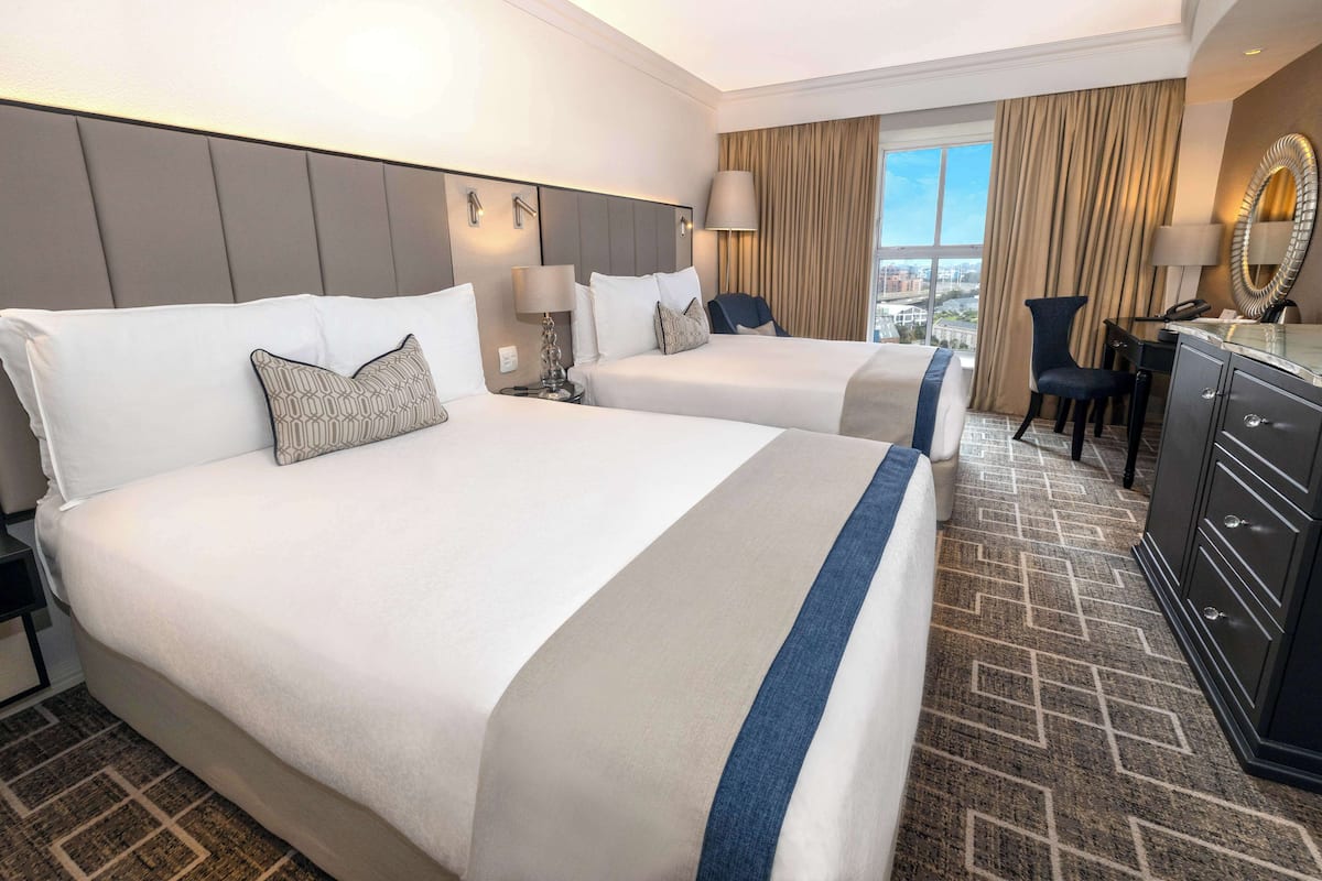 A hotel room with two beds, a desk, a chair, a dresser, and a view of the city.