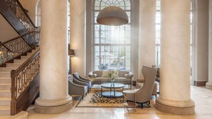 A spacious lobby with a grand staircase, large columns, and a seating area with a coffee table and chairs. - Southern Sun The Cullinan (Cape Town)