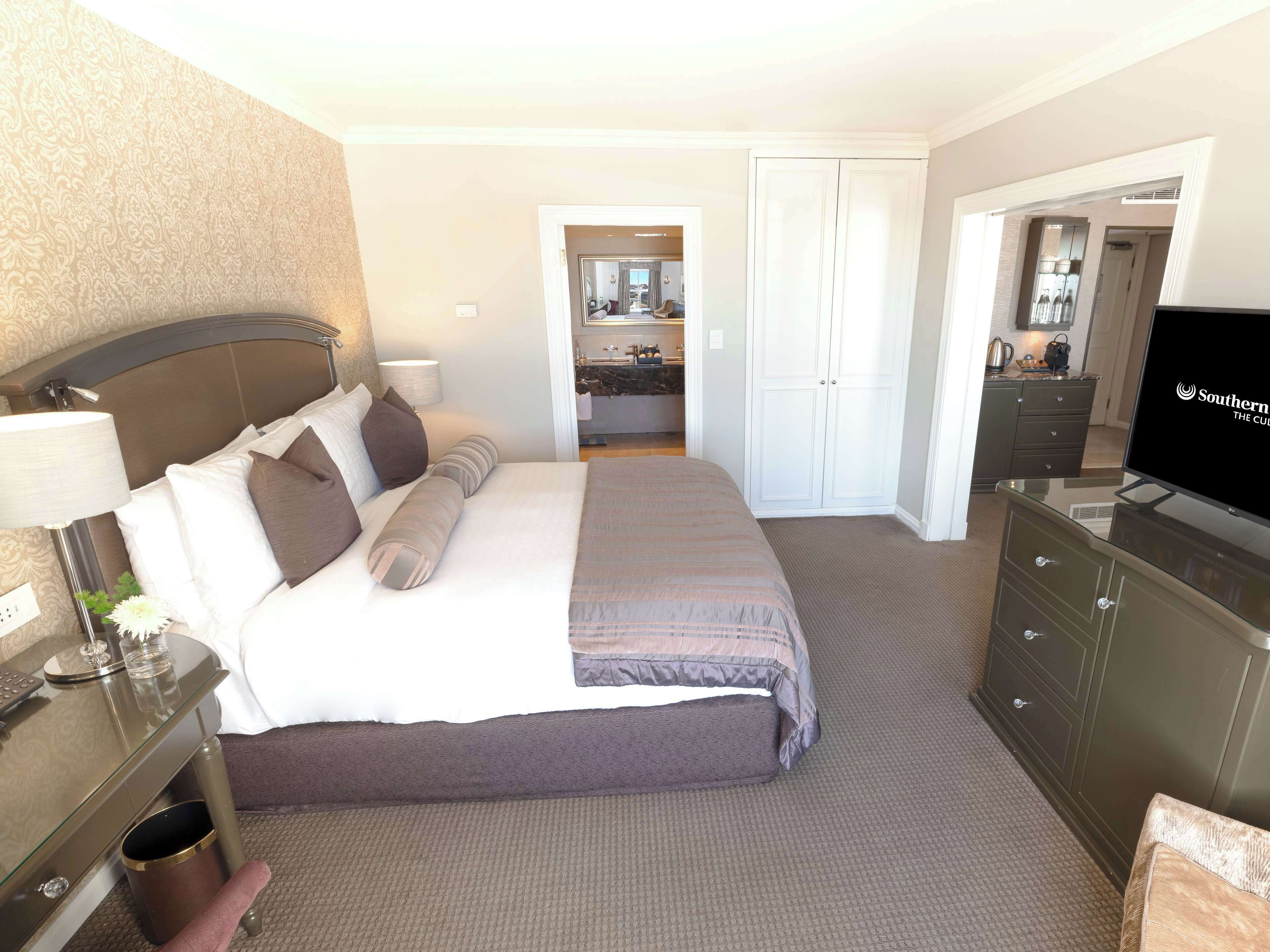 A hotel room with a bed, a desk, a TV, and a bathroom visible through an open door.