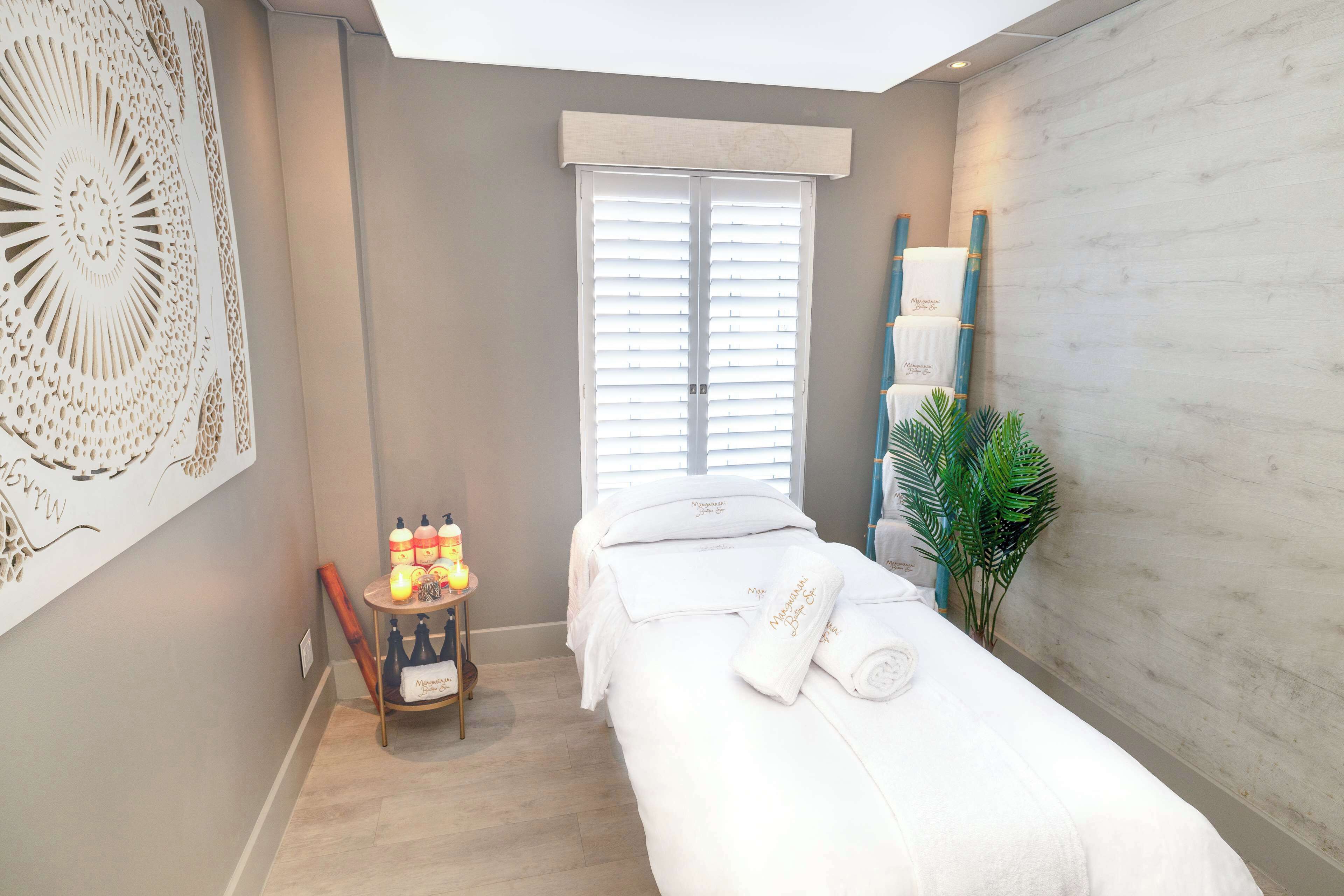 Un cuarto de spa con una camilla de masaje, una mesita con velas y botellas, y una decoración grande en la pared.