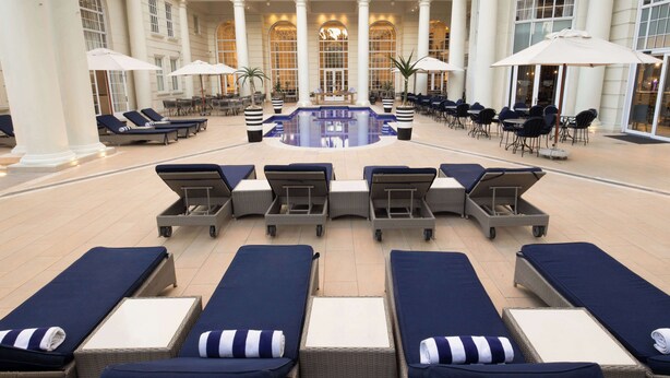 A hotel lobby with a central pool, lounge chairs, and tables with umbrellas. - Southern Sun The Cullinan (Cape Town)