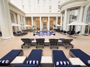 A hotel lobby with a central pool, lounge chairs, and tables with umbrellas. - Southern Sun The Cullinan (Cape Town)