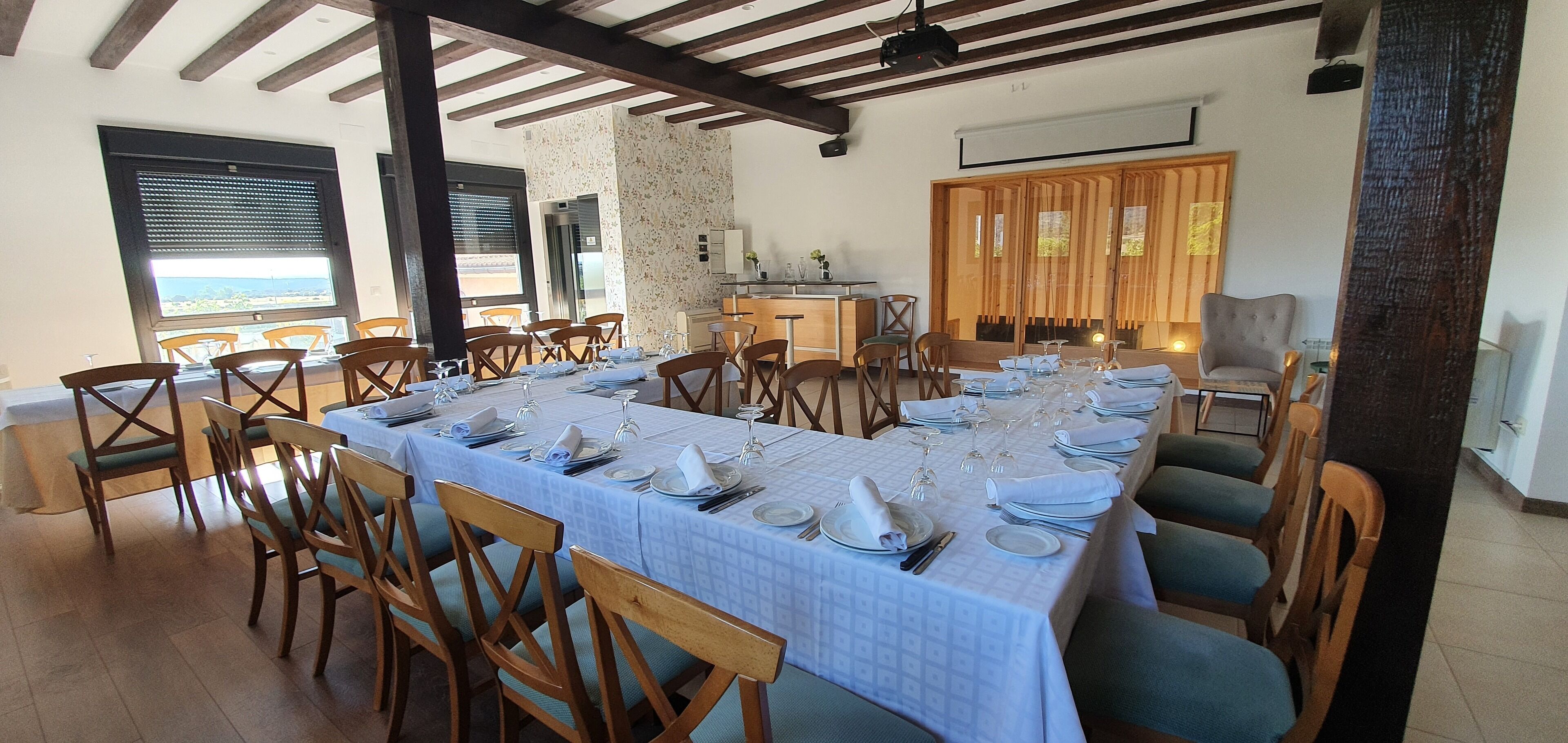 Un espace repas avec une longue table dressée pour le repas, des chaises en bois et une vue sur la mer grâce à de grandes fenêtres.