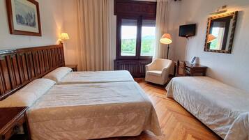 Habitación de hotel con dos camas, una silla, un escritorio con lámpara, un televisor y una ventana con cortinas.