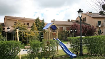 Children can play on the swing set and slide in this well-maintained playground surrounded by trees and residential buildings.
