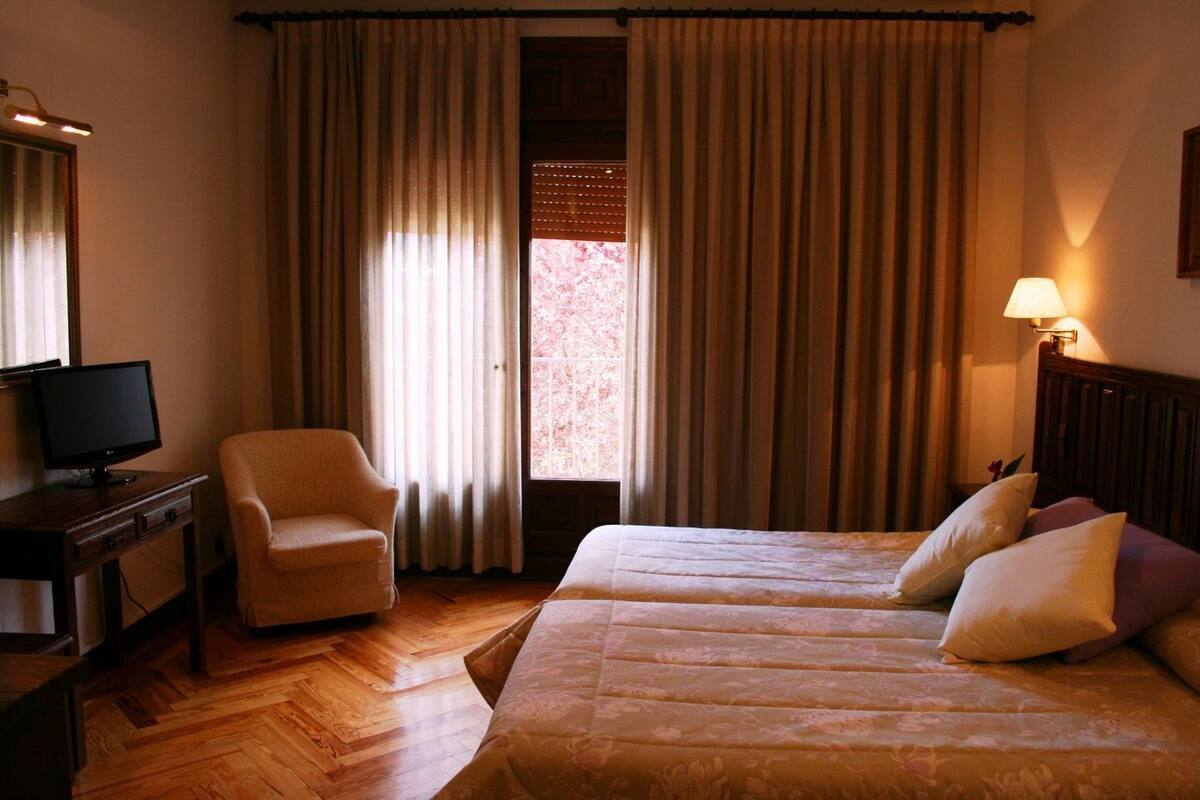 Ein Hotelzimmer mit einem Bett, einem Sessel, einem Schreibtisch mit Fernseher und einem Fenster mit Vorhängen.