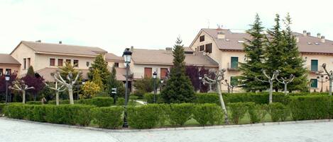 A row of residential buildings with a paved courtyard and trimmed hedges.
