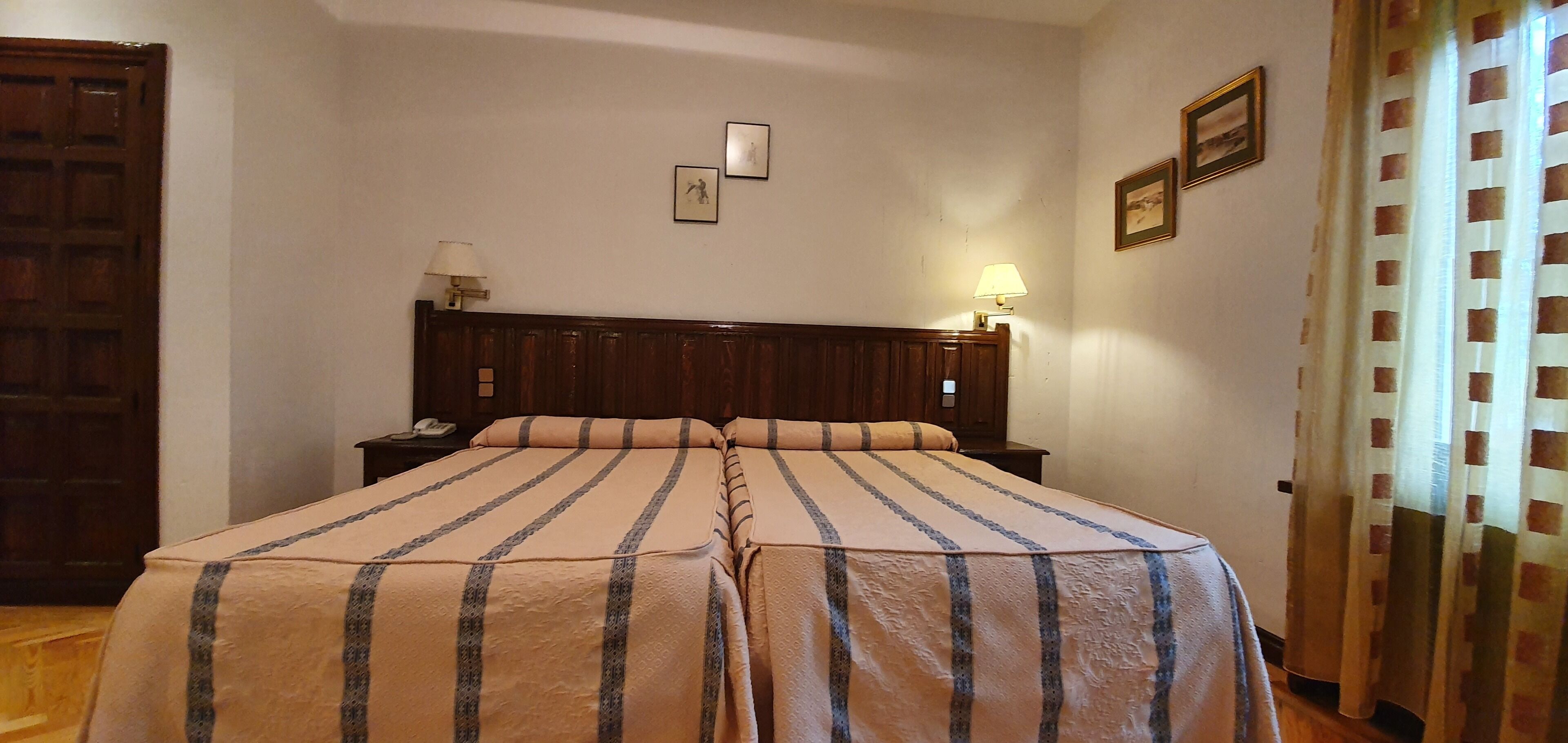 A double bed with striped bedding, a wooden headboard, bedside lamps, and a telephone on the nightstand.