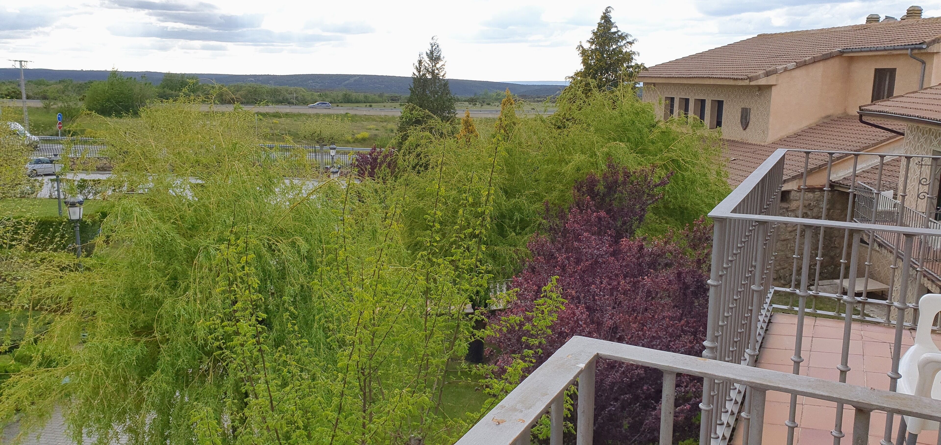 A balcony with a view of a garden and a building with a tiled roof.