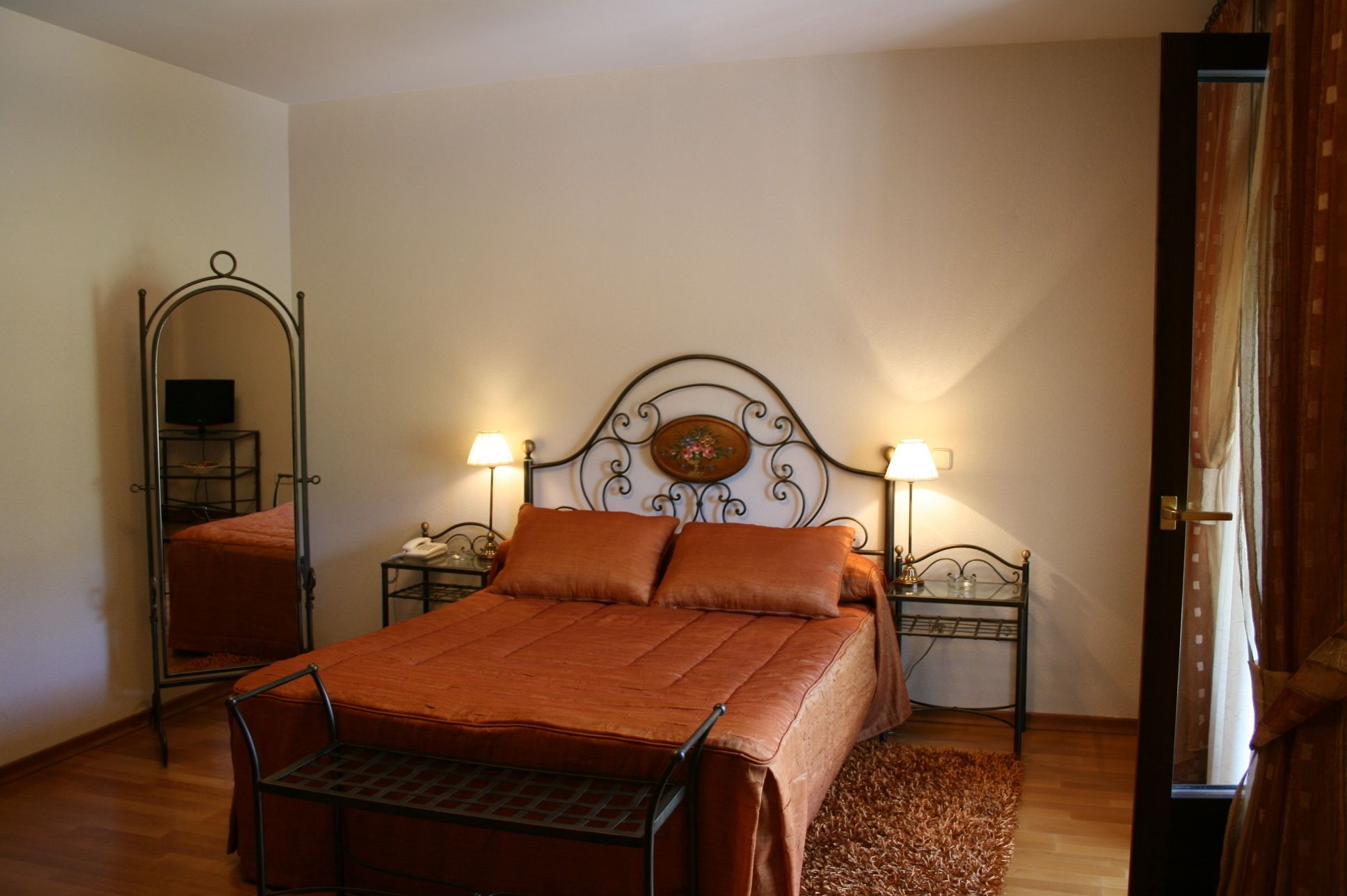 Un dormitorio con una cama, dos mesitas de noche, un espejo y una puerta.
