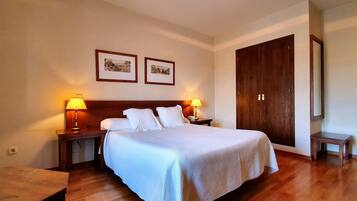 Un dormitorio con una cama grande, dos mesitas de noche con lámparas, un armario de madera y dos cuadros enmarcados en la pared.