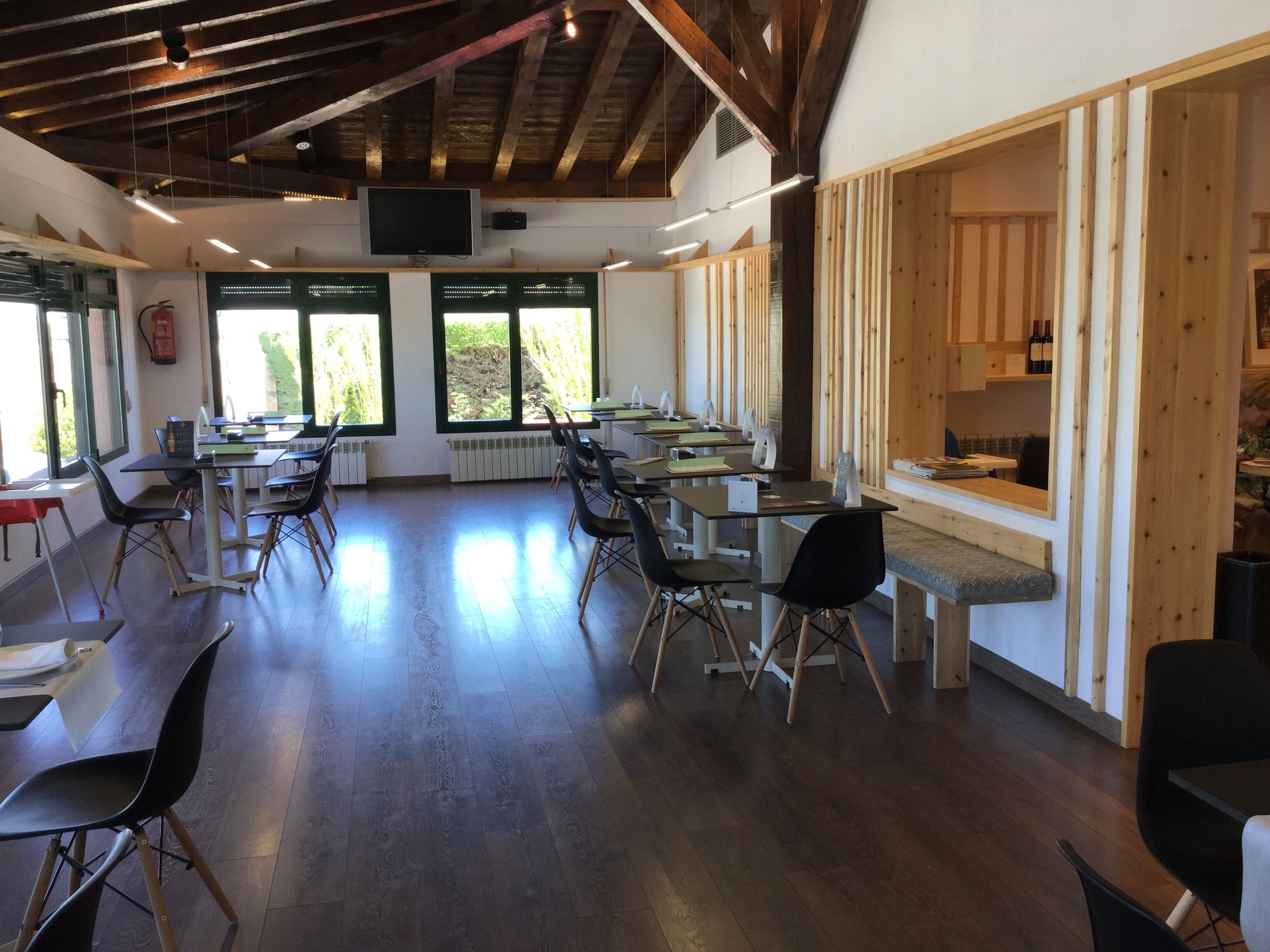 A spacious room with wooden beams on the ceiling, large windows, and multiple tables with chairs.