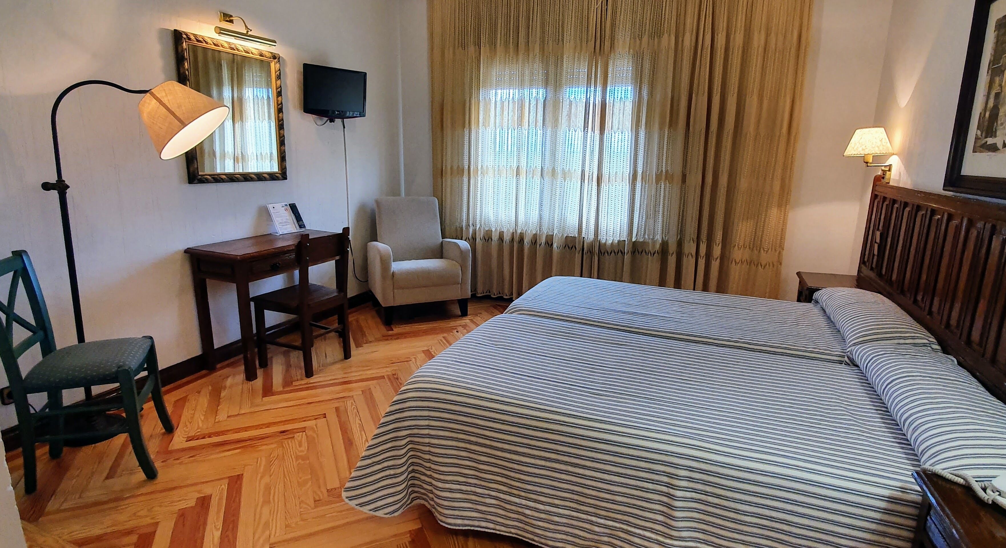 Habitación de hotel con cama, escritorio, silla, televisión y ventana con cortinas.