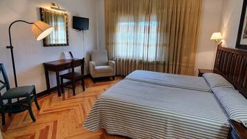Habitación de hotel con cama, escritorio, silla, televisión y ventana con cortinas.