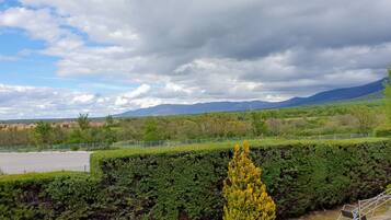 A landscape with a fenced parking area, green hedges, and distant mountains under a partly cloudy sky.
