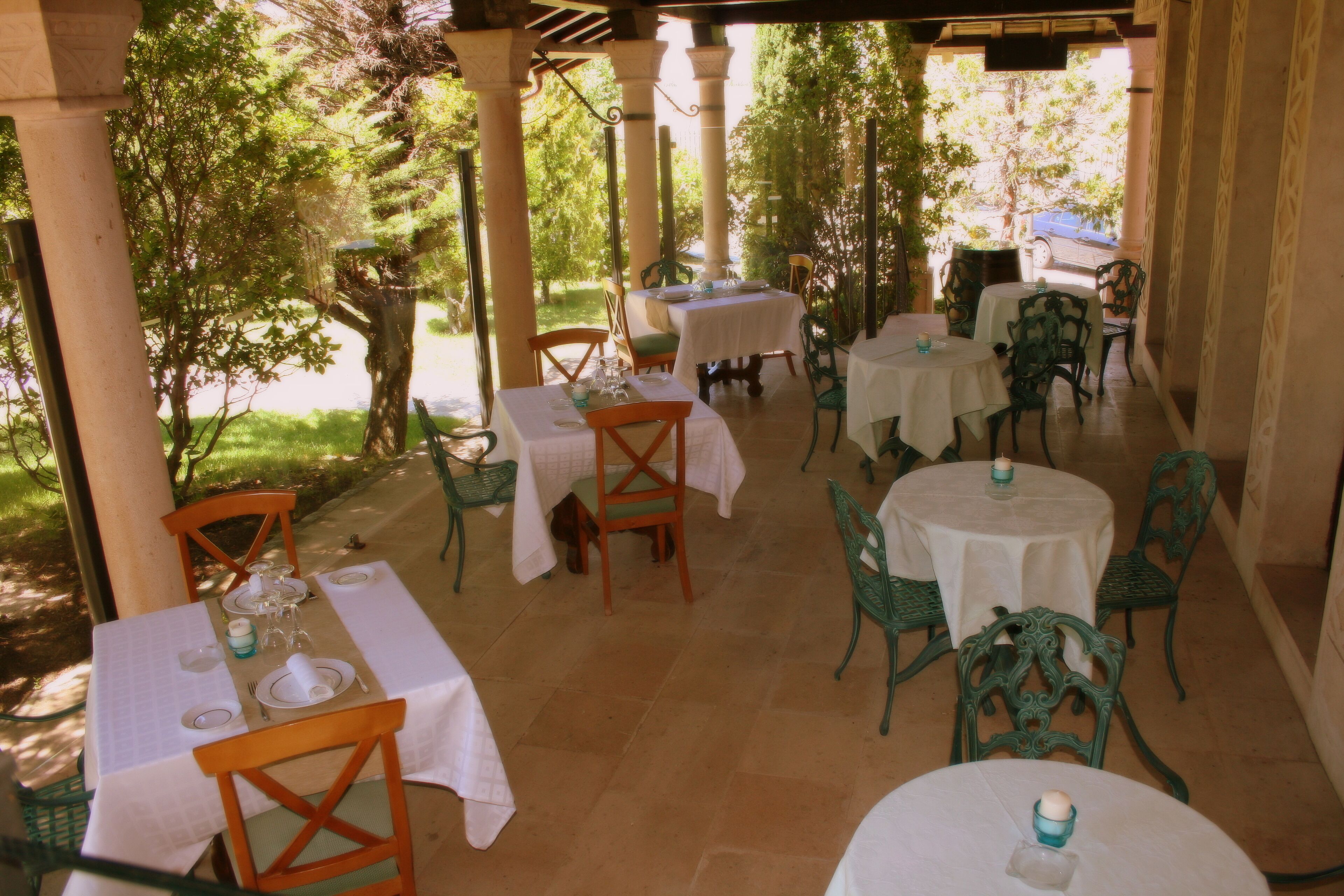 Un patio al aire libre con mesas y sillas, rodeado de árboles y columnas.