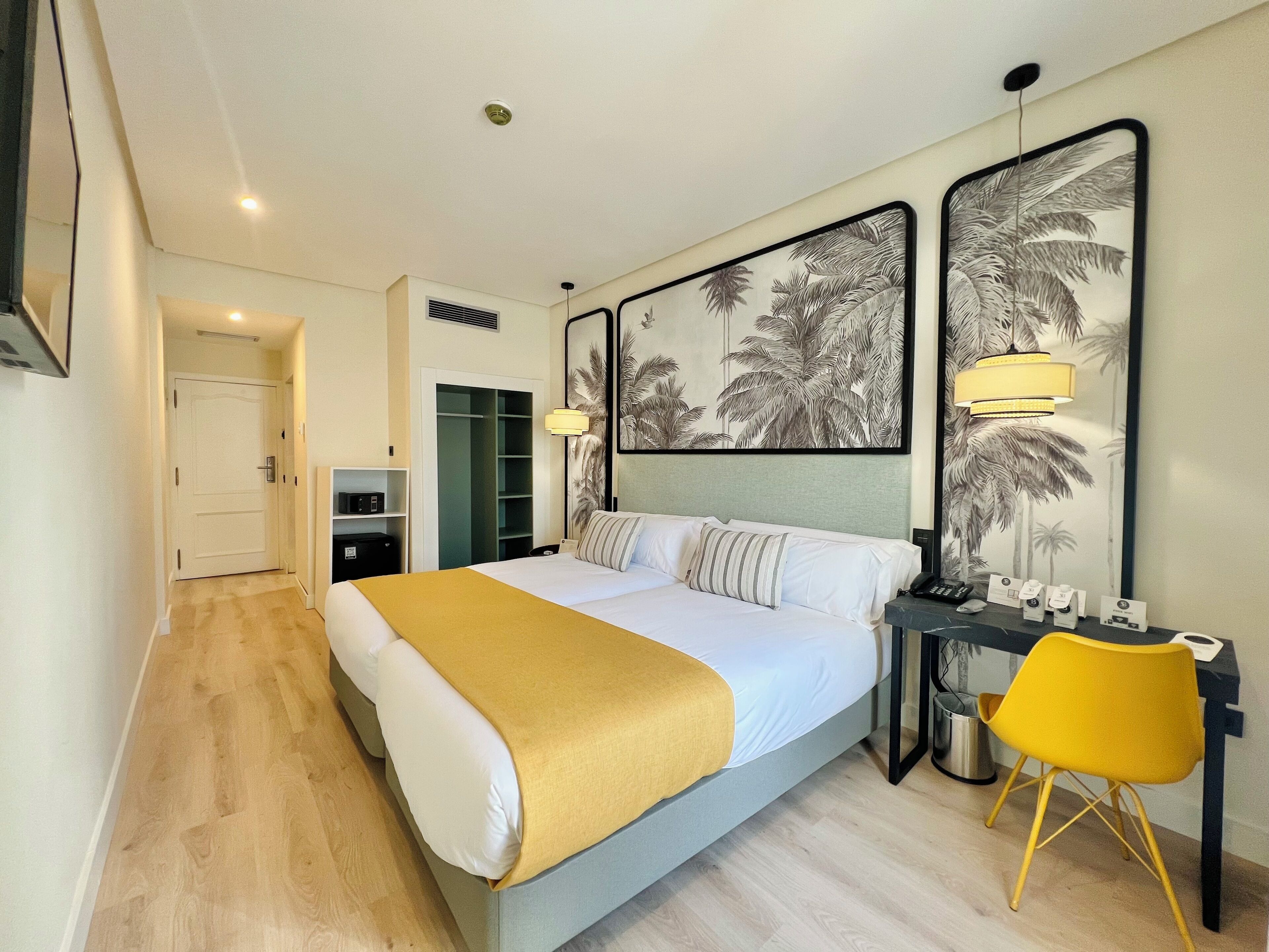 Een hotelkamer met een bed, een bureau met stoel, een kledingkast en twee foto's in lijsten aan de muur.