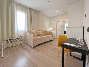 Una sala moderna con sofá, una mesa de comedor y una silla. Hay una ventana con cortinas, una lámpara sobre la mesa y un perchero.